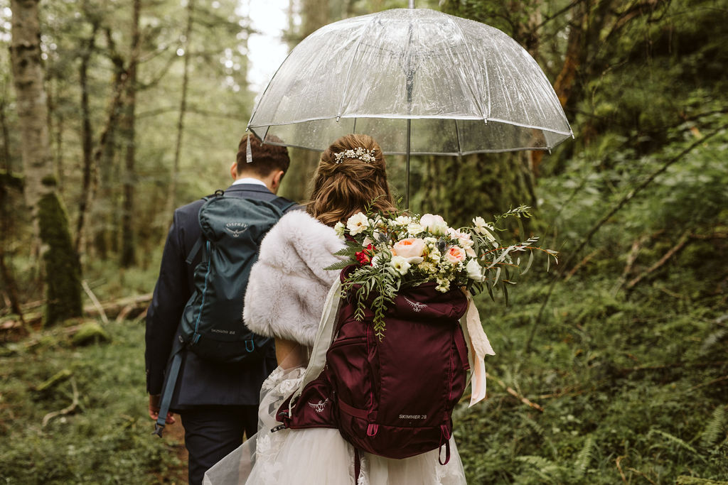 bride and groom walk through forest with backpacks during elopement
