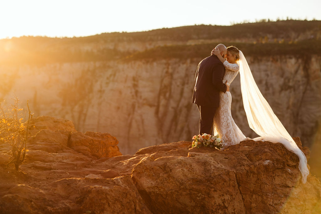 bride and groom pose in sunlight on cliffside during elopement