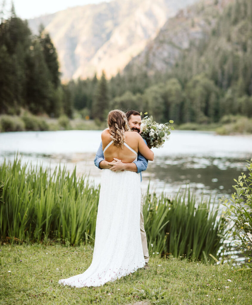 bride and groom hug in front of river by leavenworth