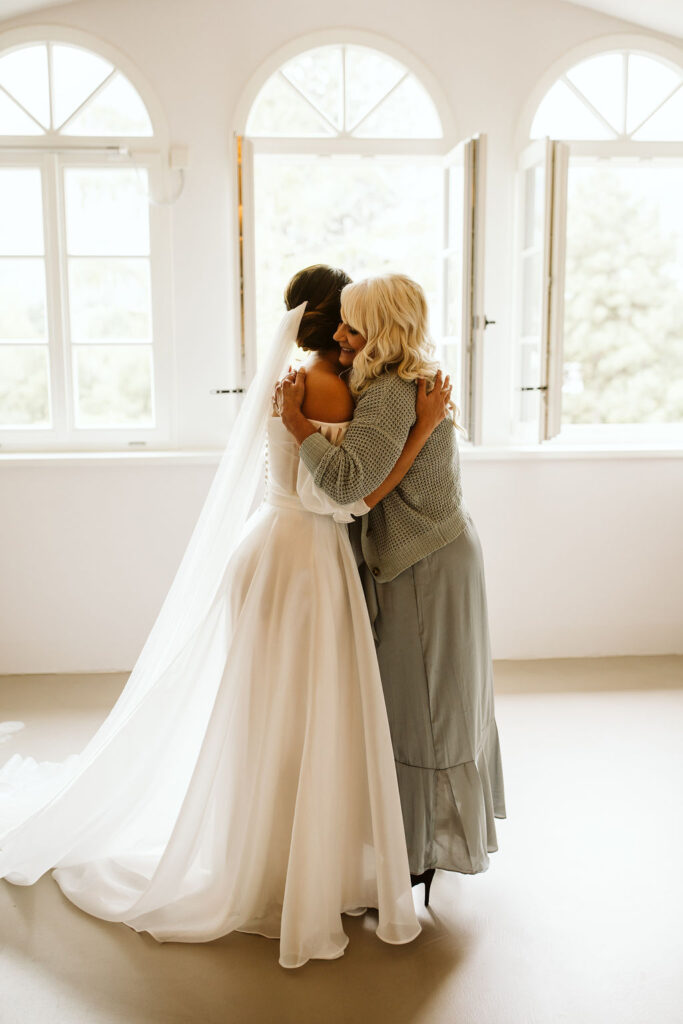 bride and her mom hug in front of a window