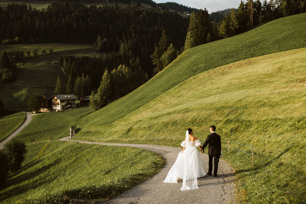 bride and groom hold hands and walk down path together with lush green hills in the back