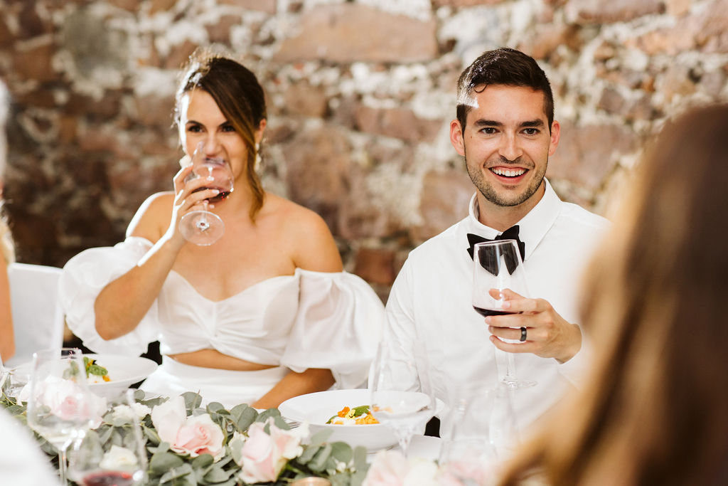 bride and groom smile while holding wine glasses