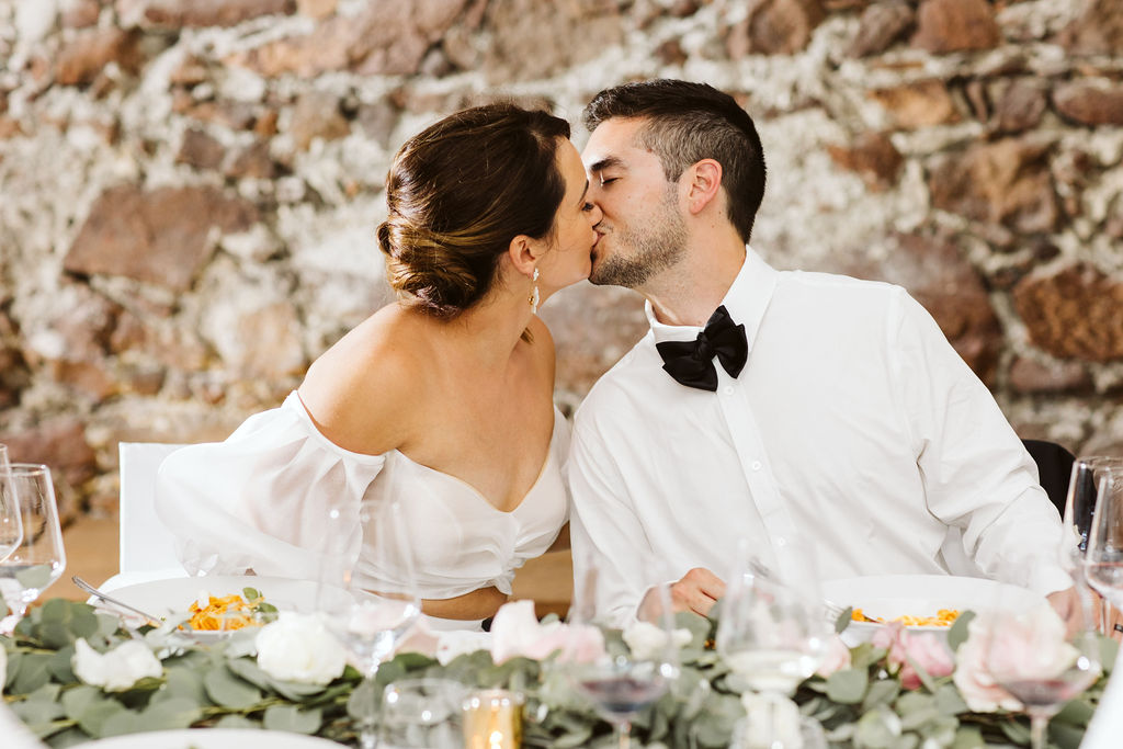 bride and groom kiss while sitting at a table next to each other
