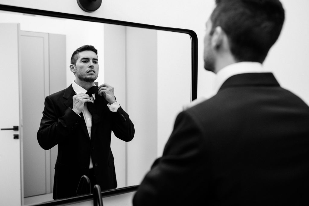 groom straightens tie while he looks in mirror