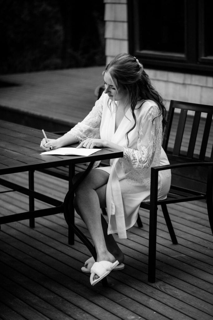 bride in robe sits at a table writing in notebook