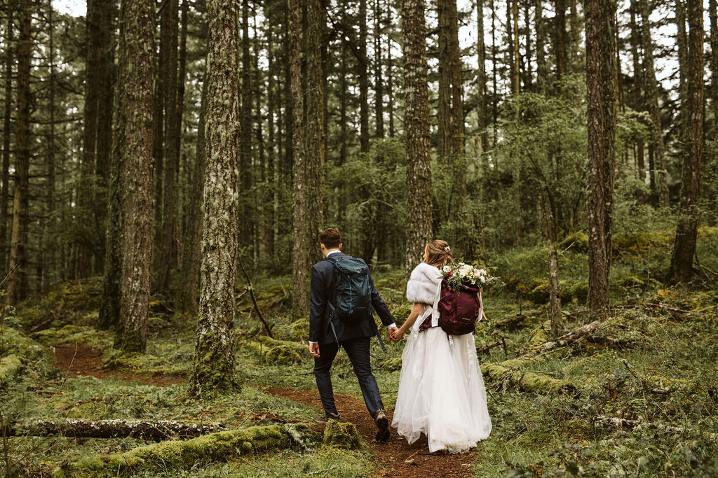 bride and groom walk through forest hand in hand
