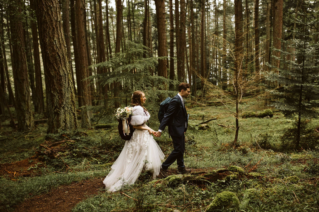 bride and groom hold hands and walk on hiking trail through forest