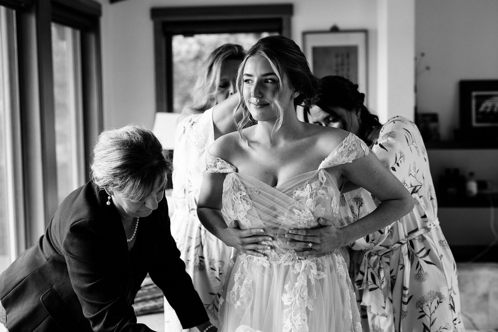 women surround bride helping her put on dress