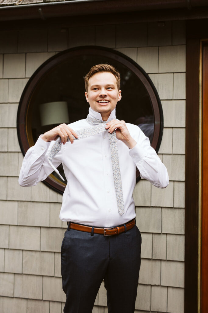 groom smiles while putting on tie