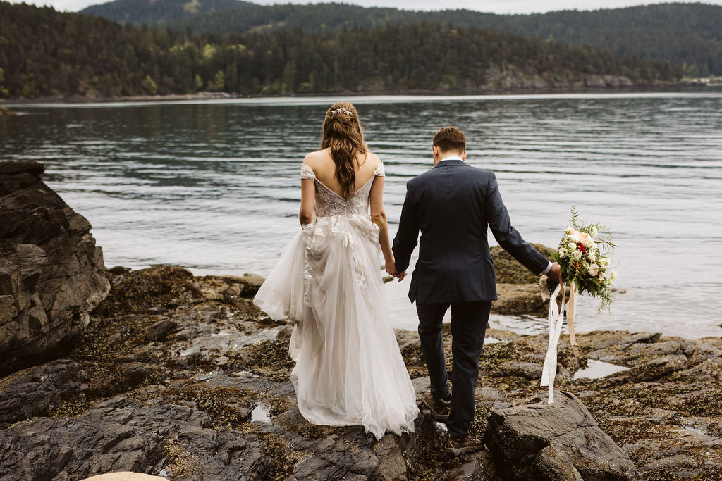 bride and groom walk along rocks near the ocean