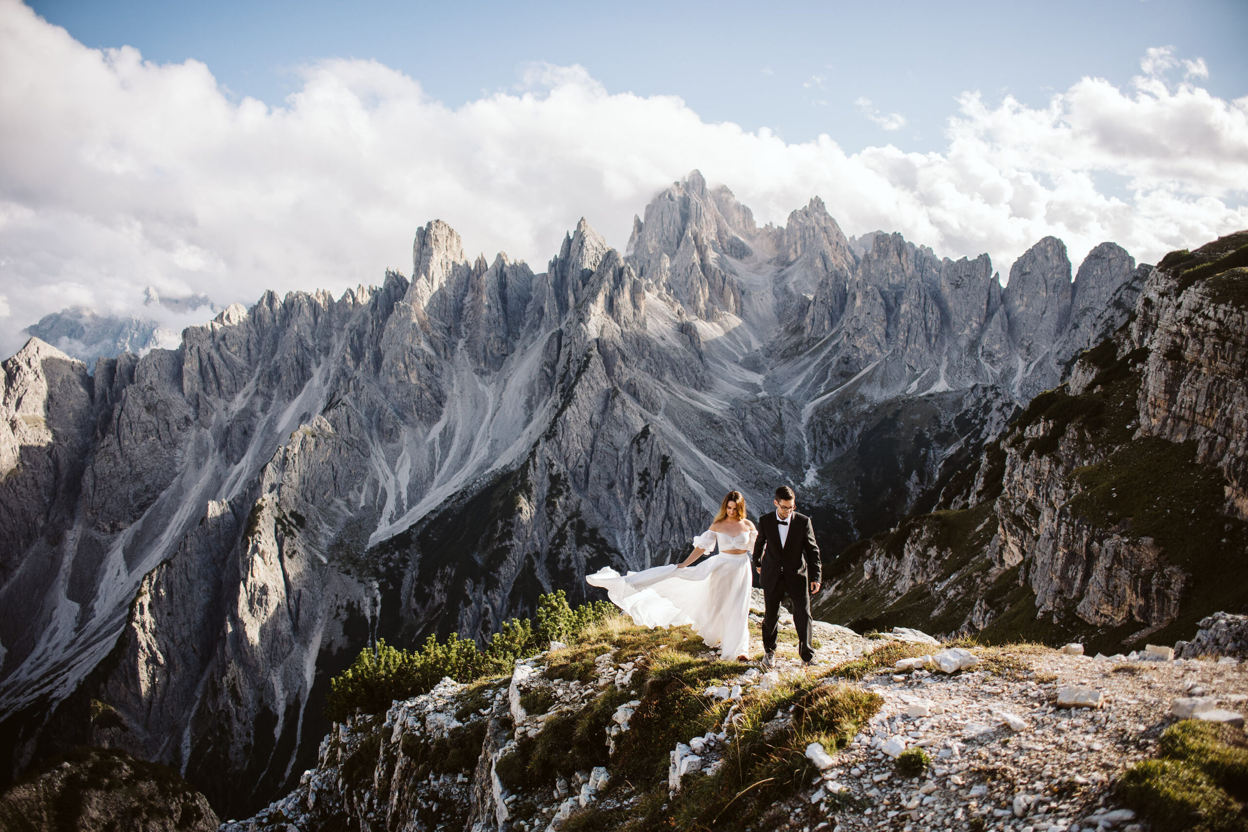 a bride and groom walking along the Dolomites mountains