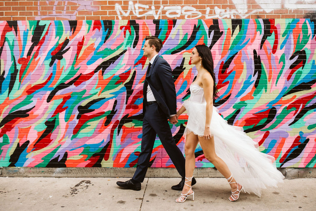 bride and groom walk past bright city wall