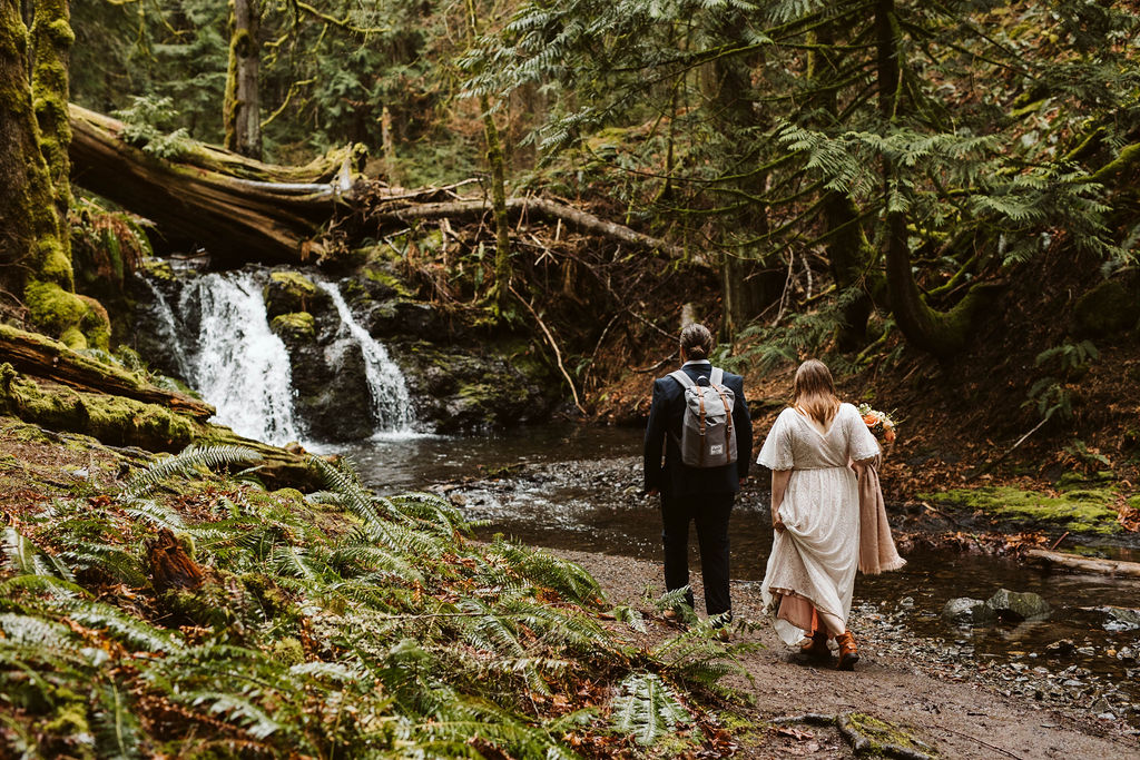 groom and bride walk through forests towards a waterfall