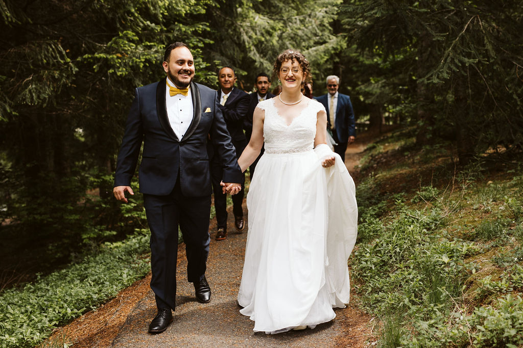 bride and groom walk down trail with guests behind them