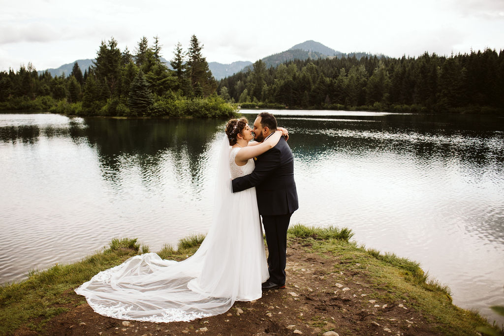 bride and groom embrace in front of lake