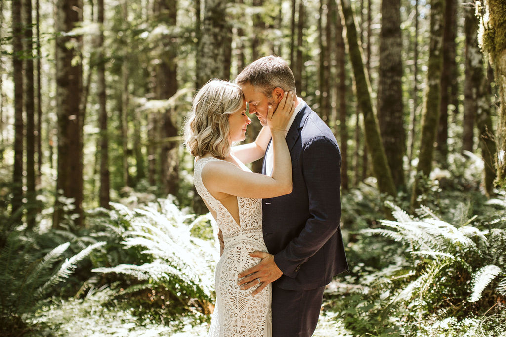 bride and groom stand in woods touching foreheads