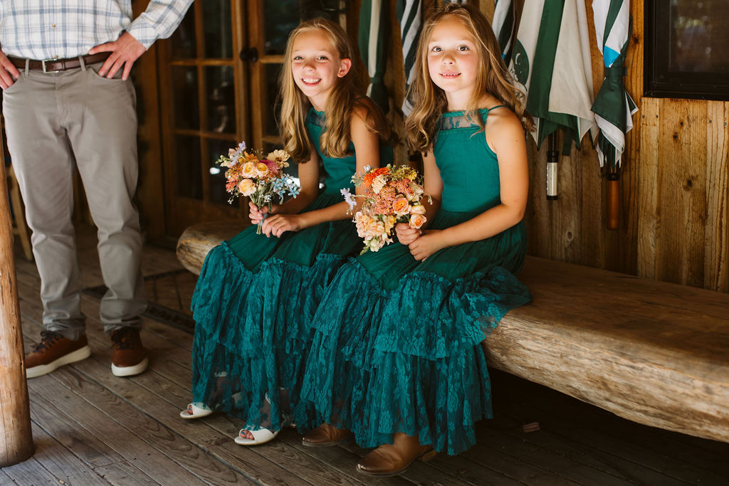 two little girls in green dresses sit on bench outside home