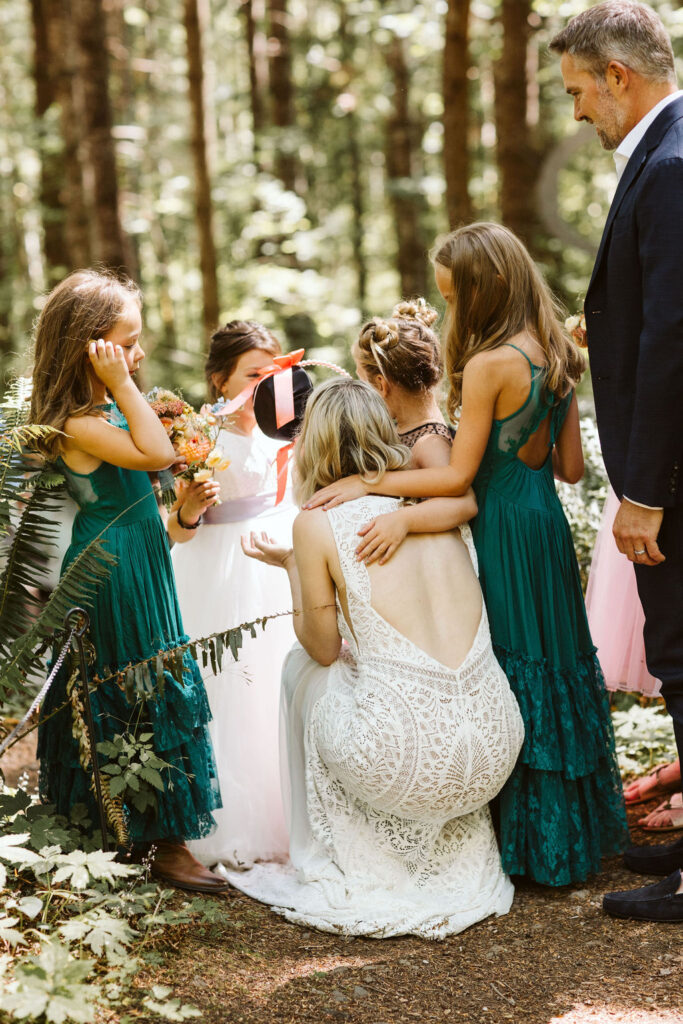 bride kneels on ground and chats with little girls