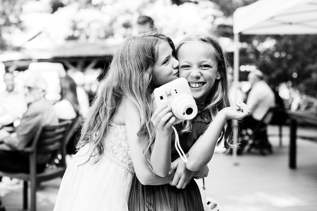 two little girls hug while holding a polaroid camera
