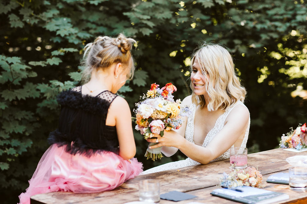 bride holds out wildflower bouquet to little girl