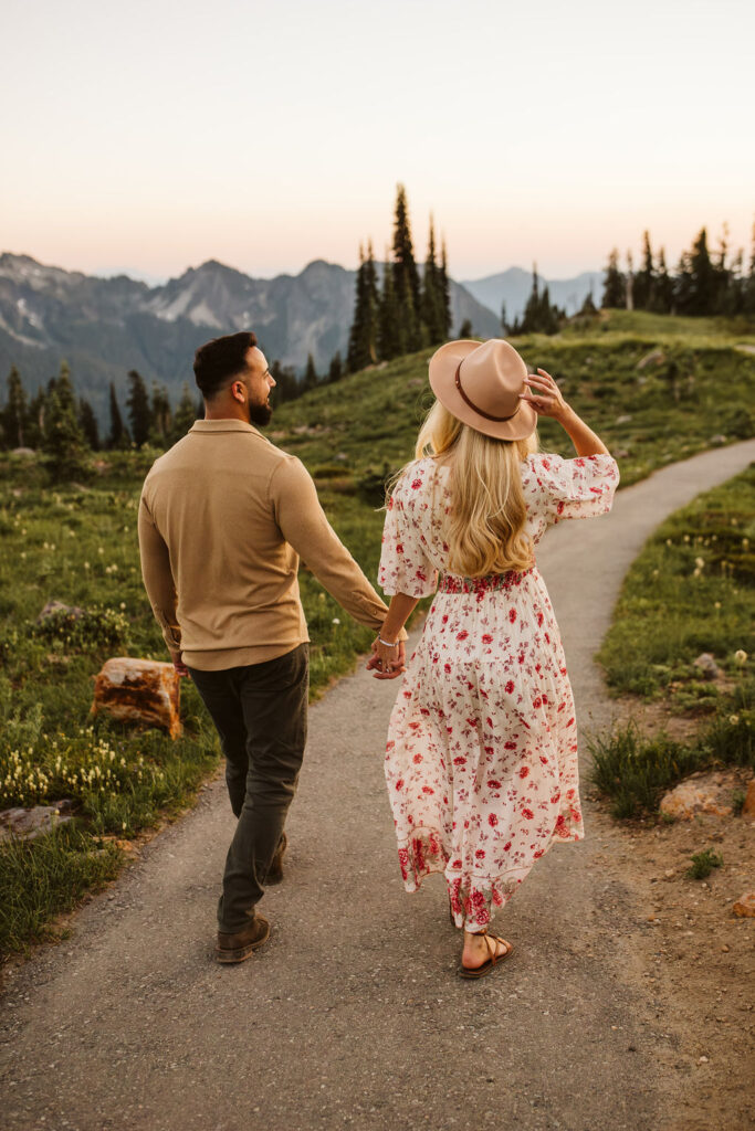 man and woman walk down path while woman holds her hat on