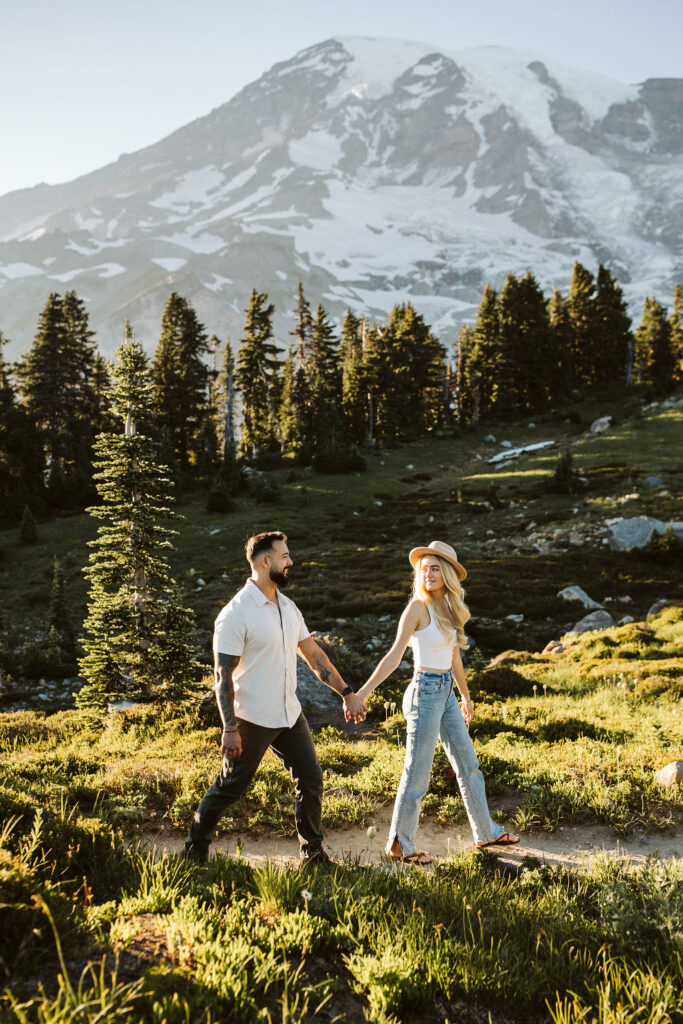 boy and girl walk through meadows at mt rainier engagement session