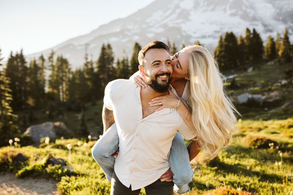 girl is on boys back and reaches around to kiss his cheek at mt rainier engagement session