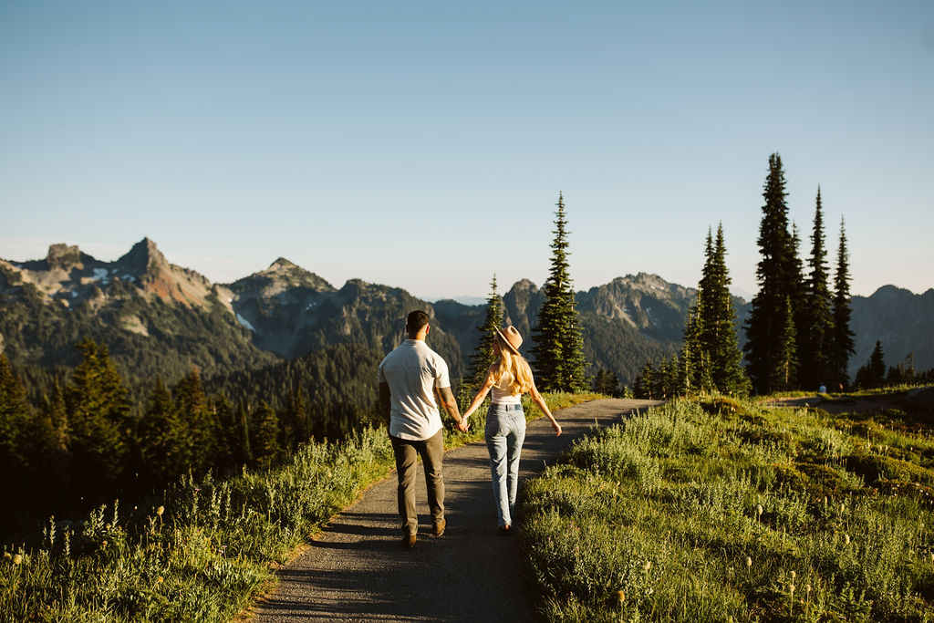 boy and girl walk down gravel path between meadows at mt rainier engagement session