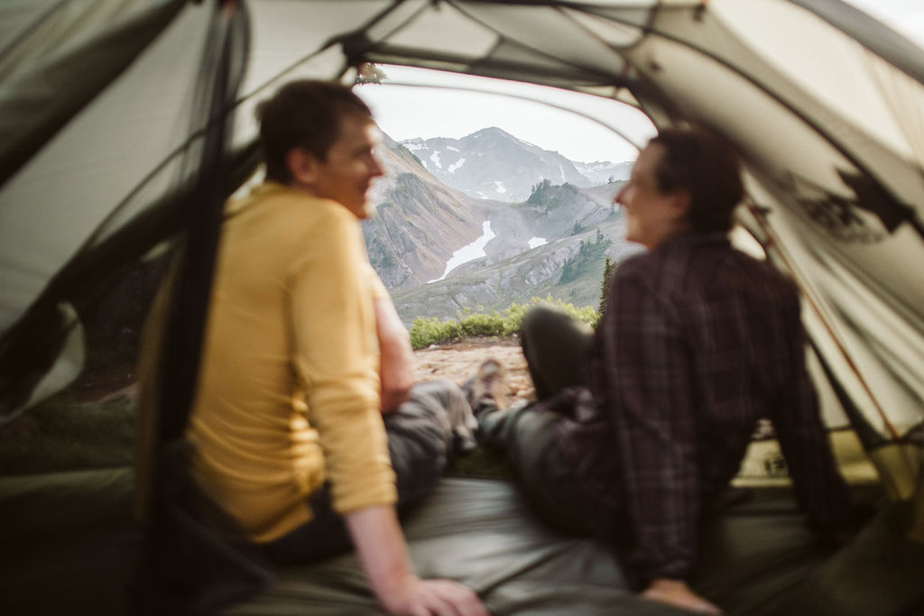 man and woman sit in entrance of tent looking at each other
