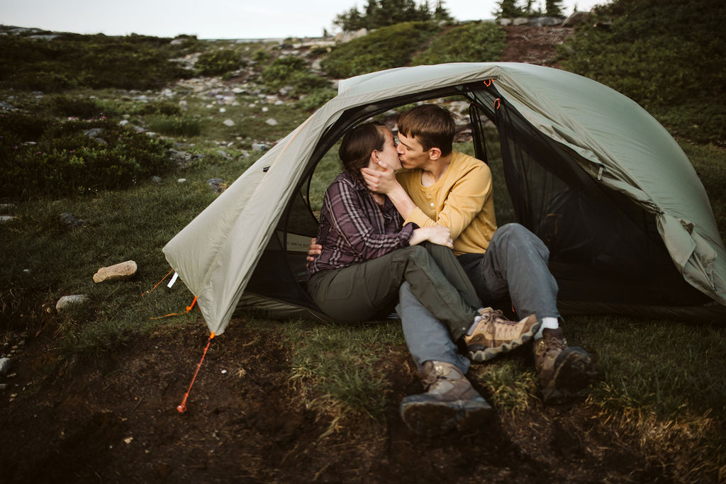 man and woman kiss while sitting in the opening of tent