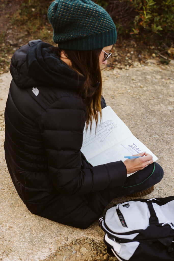 woman sits on rock and journals